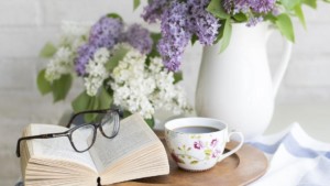 Pöydällä avonainen kirja, kahvikuppi ja maljakollinen kukkia