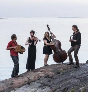Kuvassa neljä muusikkoa meren rannalla.