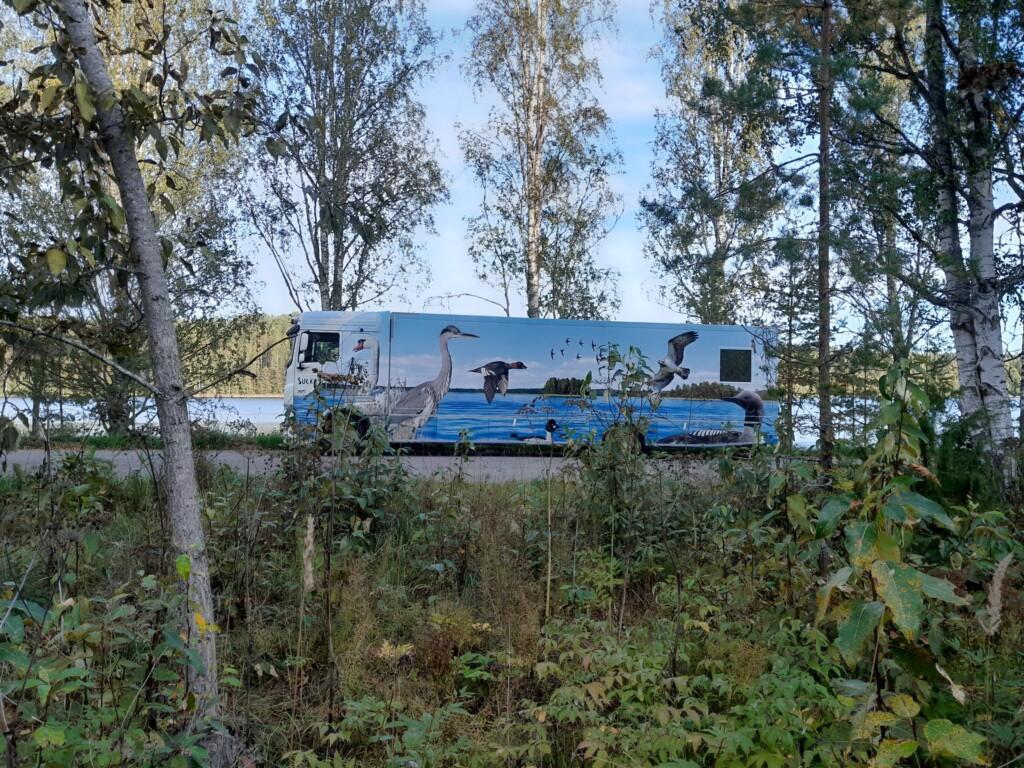 Kirjastoauto Sulka puiden takana rannalla